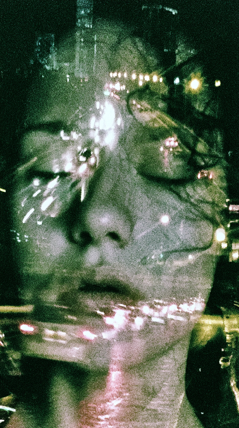 A double-exposed portrait, a face layered with city light